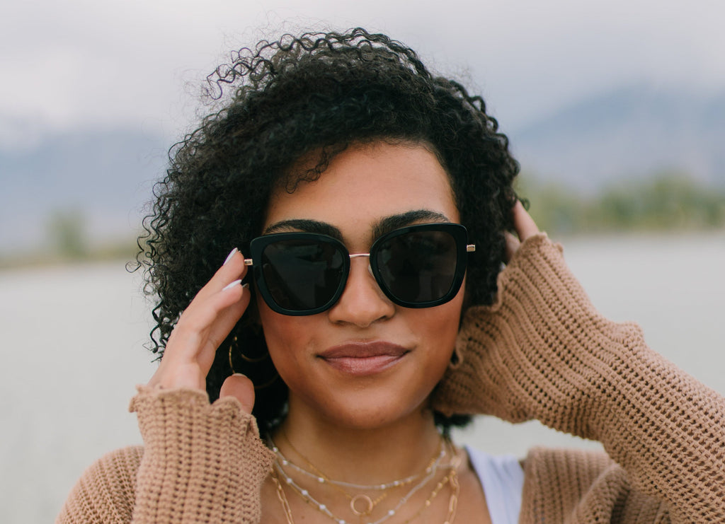 Woman wearing sunglasses and a beige cardigan outdoors with a blurred natural background