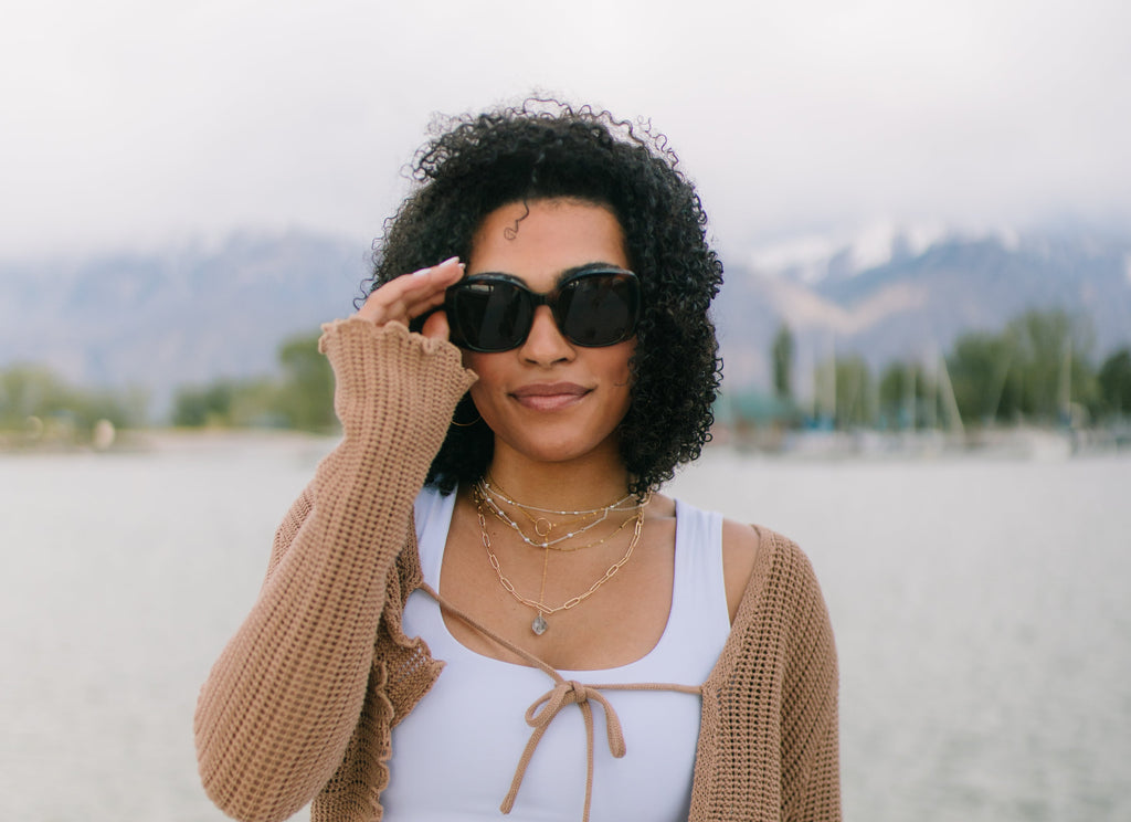 Woman wearing sunglasses and a beige cardigan on a beach
