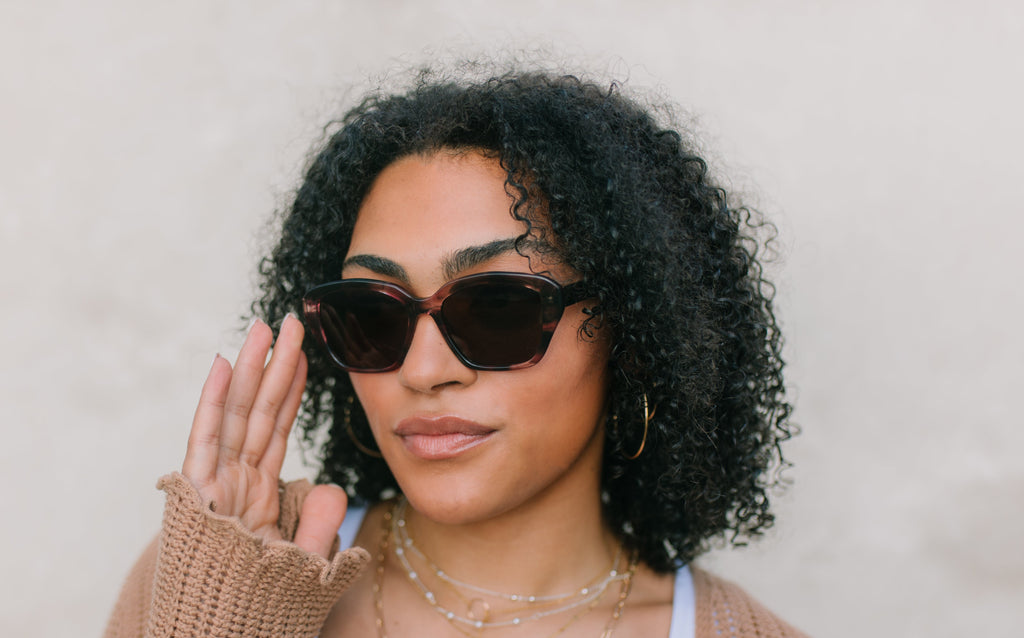 Woman wearing sunglasses and a beige cardigan against a plain background