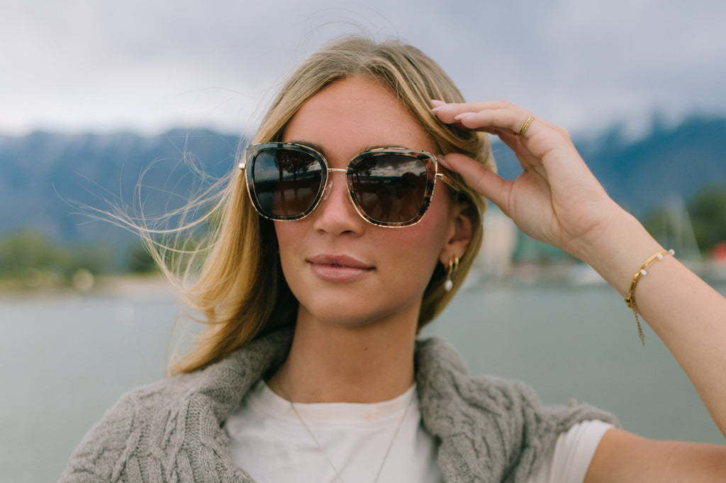 Woman wearing sunglasses and a gray scarf with a scenic background
