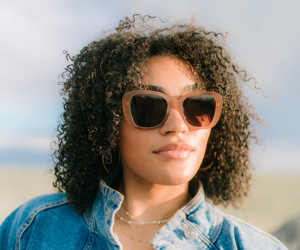 Woman wearing sunglasses and a denim jacket with a blurred background