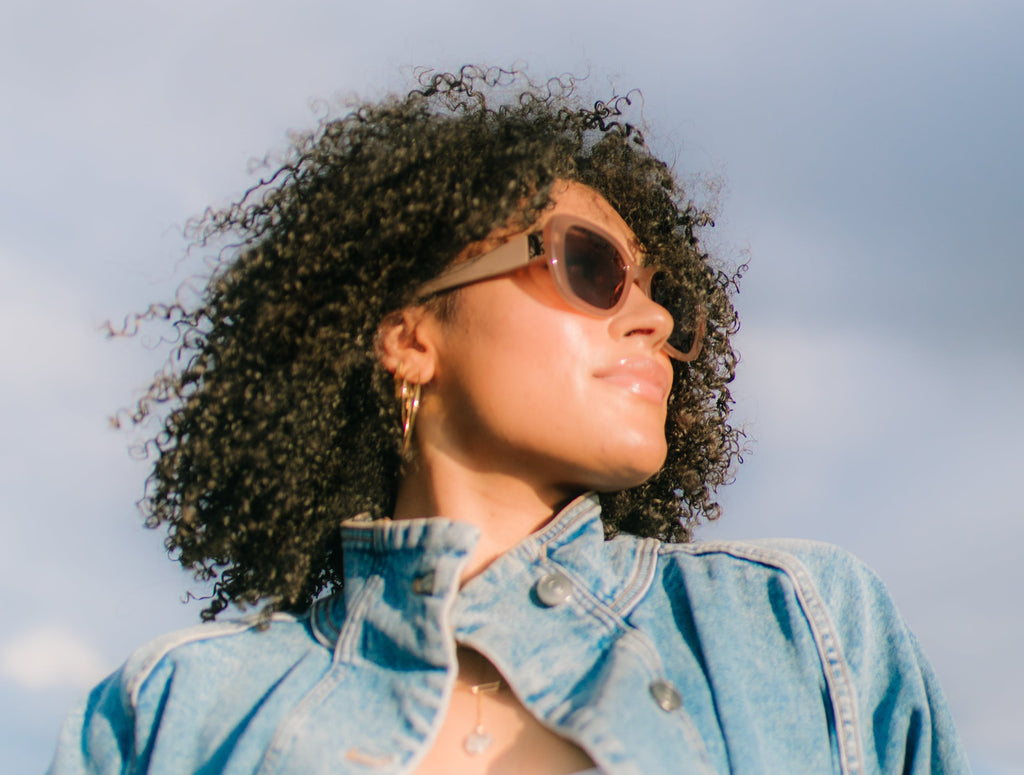 Woman wearing sunglasses and a denim jacket against a cloudy sky