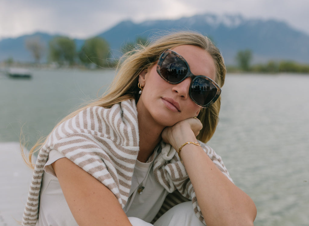 Woman sitting on a dock by a lake with mountains in the background