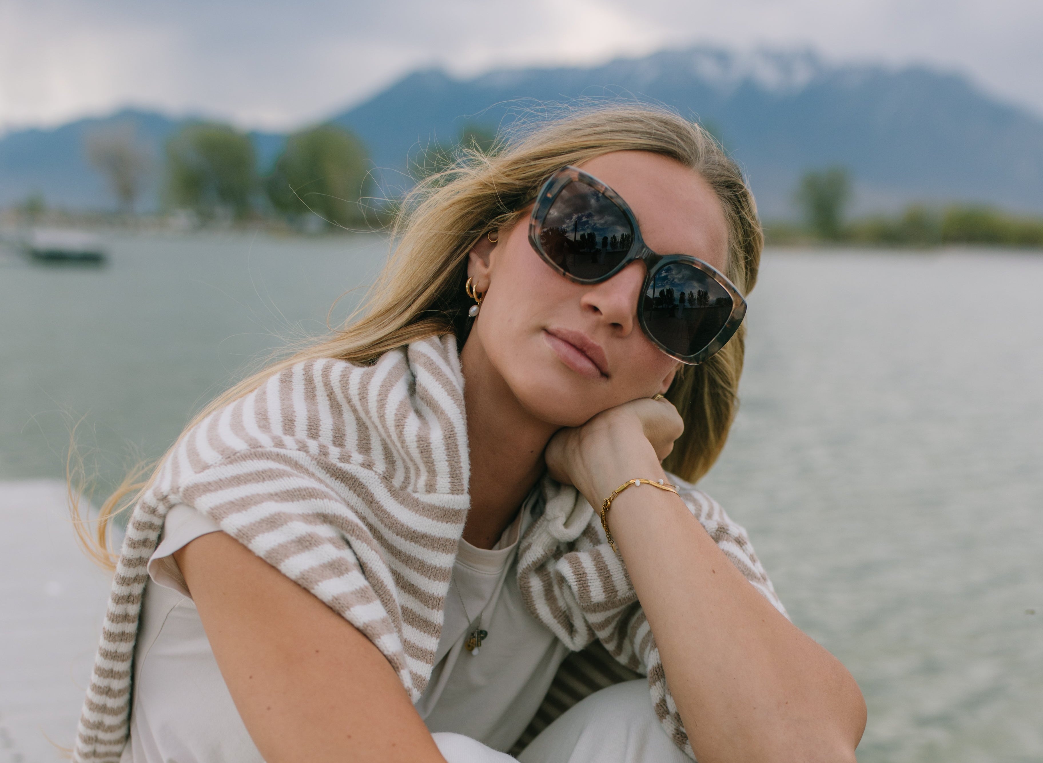 Woman sitting on a dock by a lake with mountains in the background