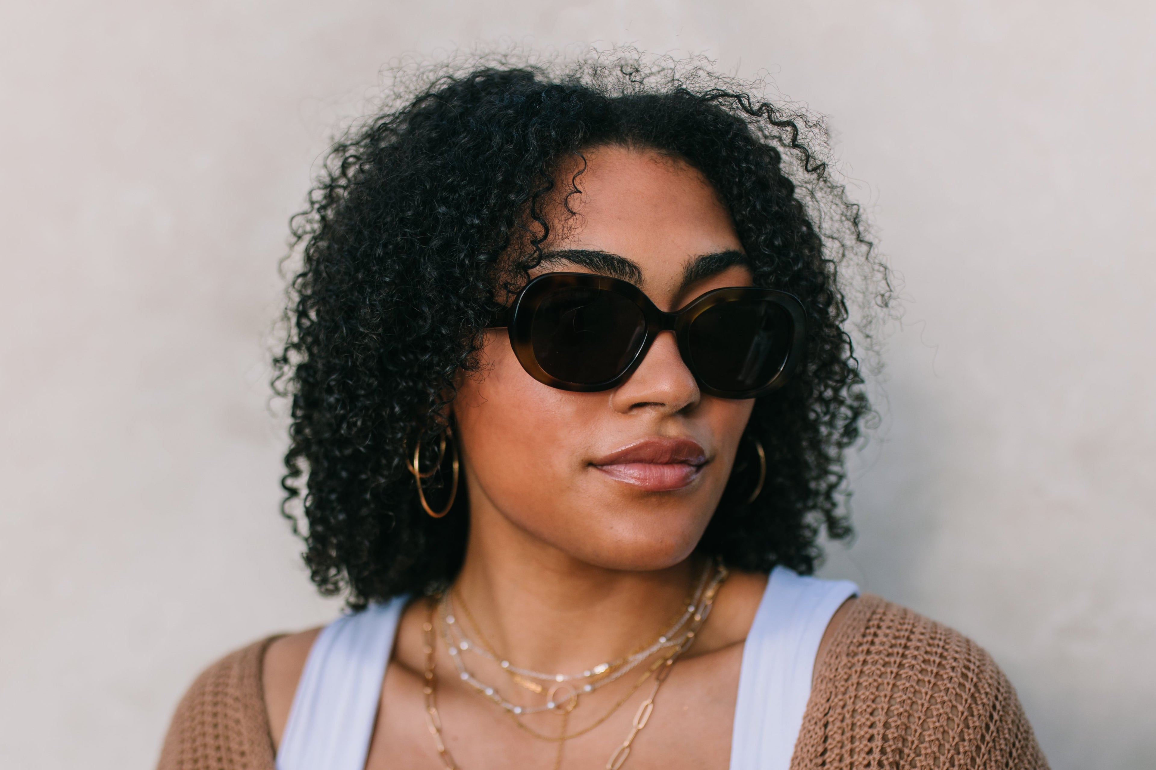 Woman wearing sunglasses and a brown cardigan against a neutral background