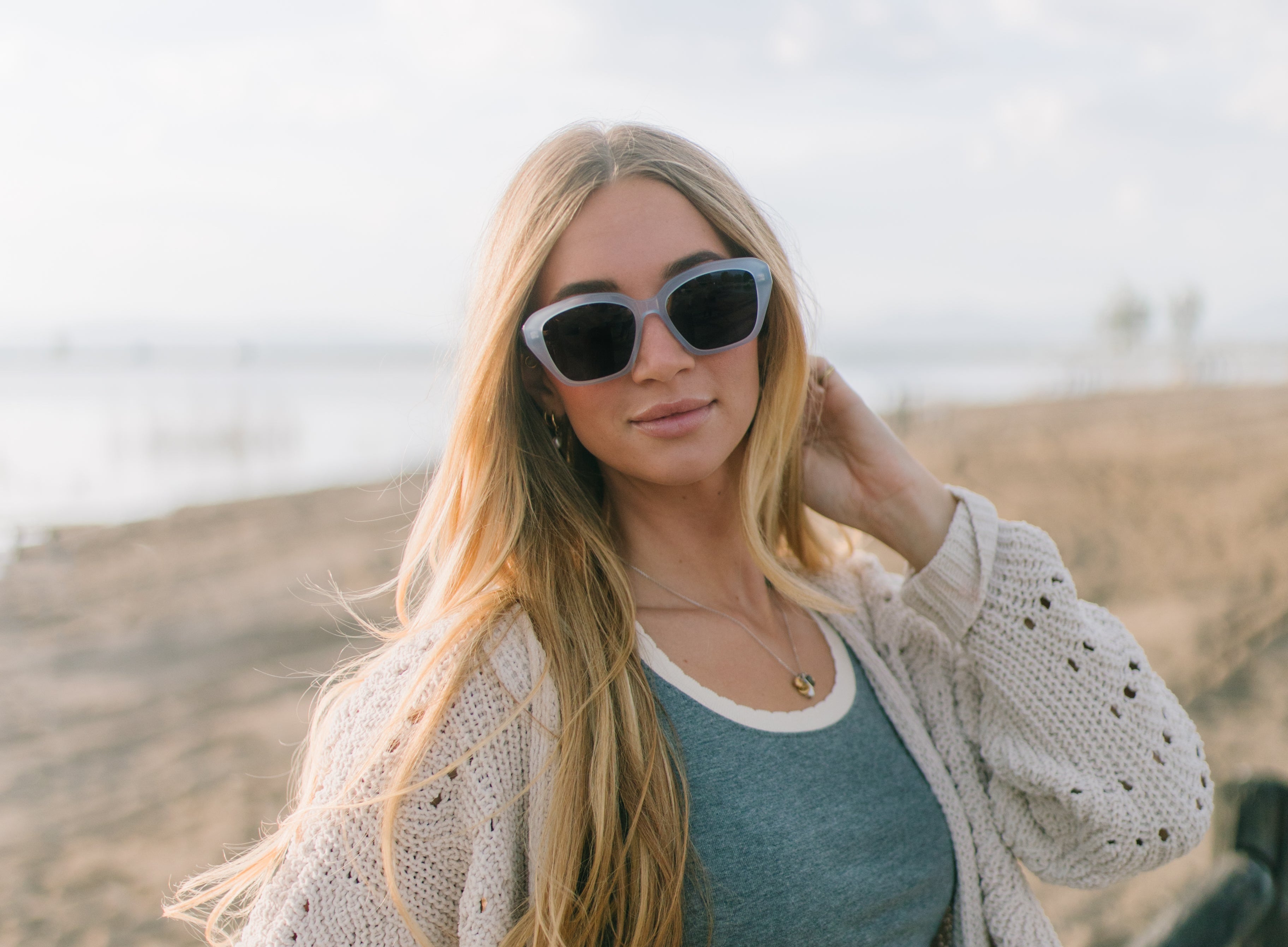 Woman wearing sunglasses and a cardigan on a beach