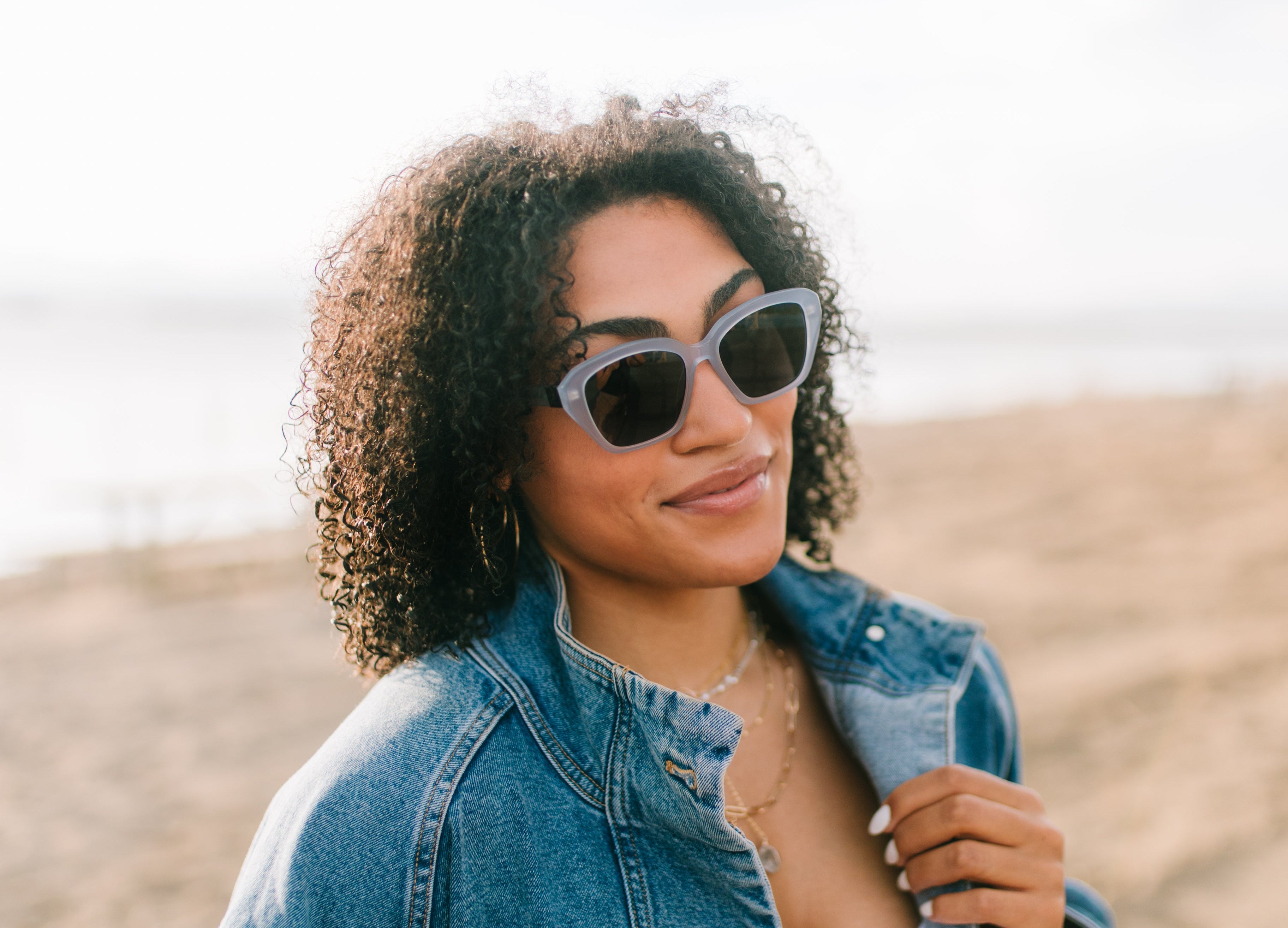 Woman wearing a denim jacket and sunglasses on a beach